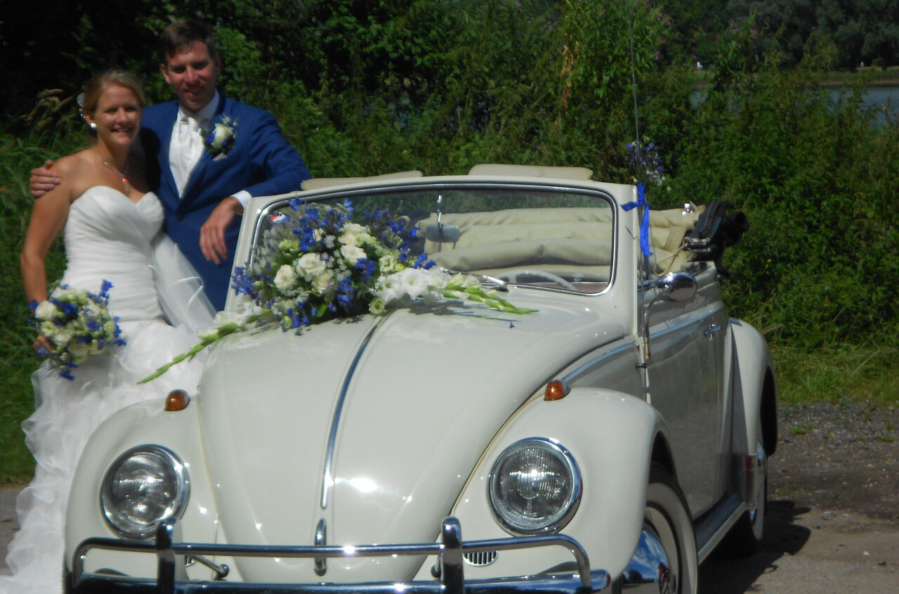 Bruidspaar bij de crèmekleurige VW Kever cabrio 1963 met bloemen op de motorkap.