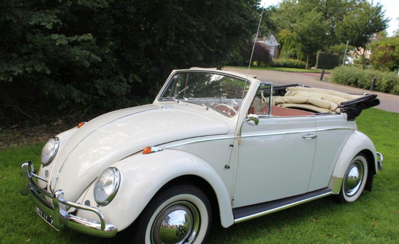Crèmekleurige VW Kever cabrio uit 1963 met opengevouwen dak, schuin van voren op een grasveld.
