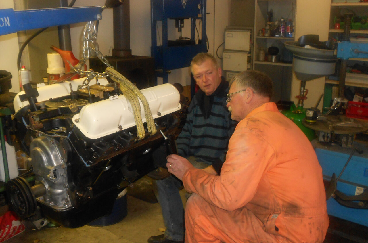 Jan en een monteur bij de gereviseerde V8-motor van de Thunderbird, hangend aan een takel in de werkplaats.