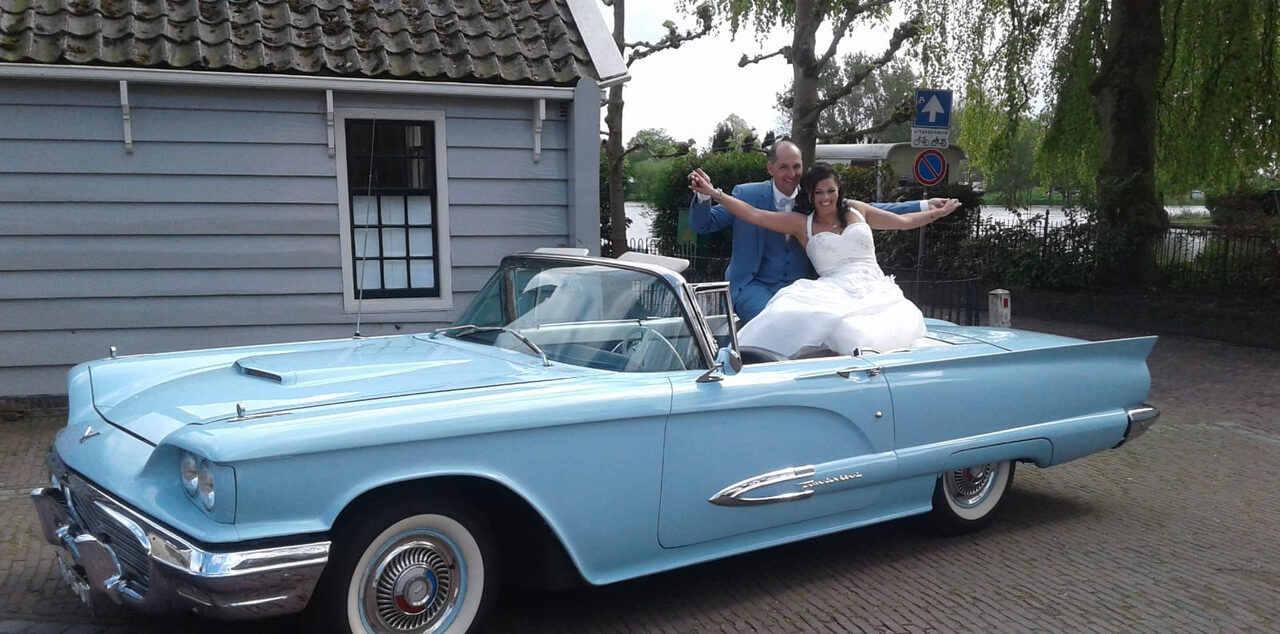 Bruidspaar zit achterin de open Ford Thunderbird 1959 op een mooie dag.