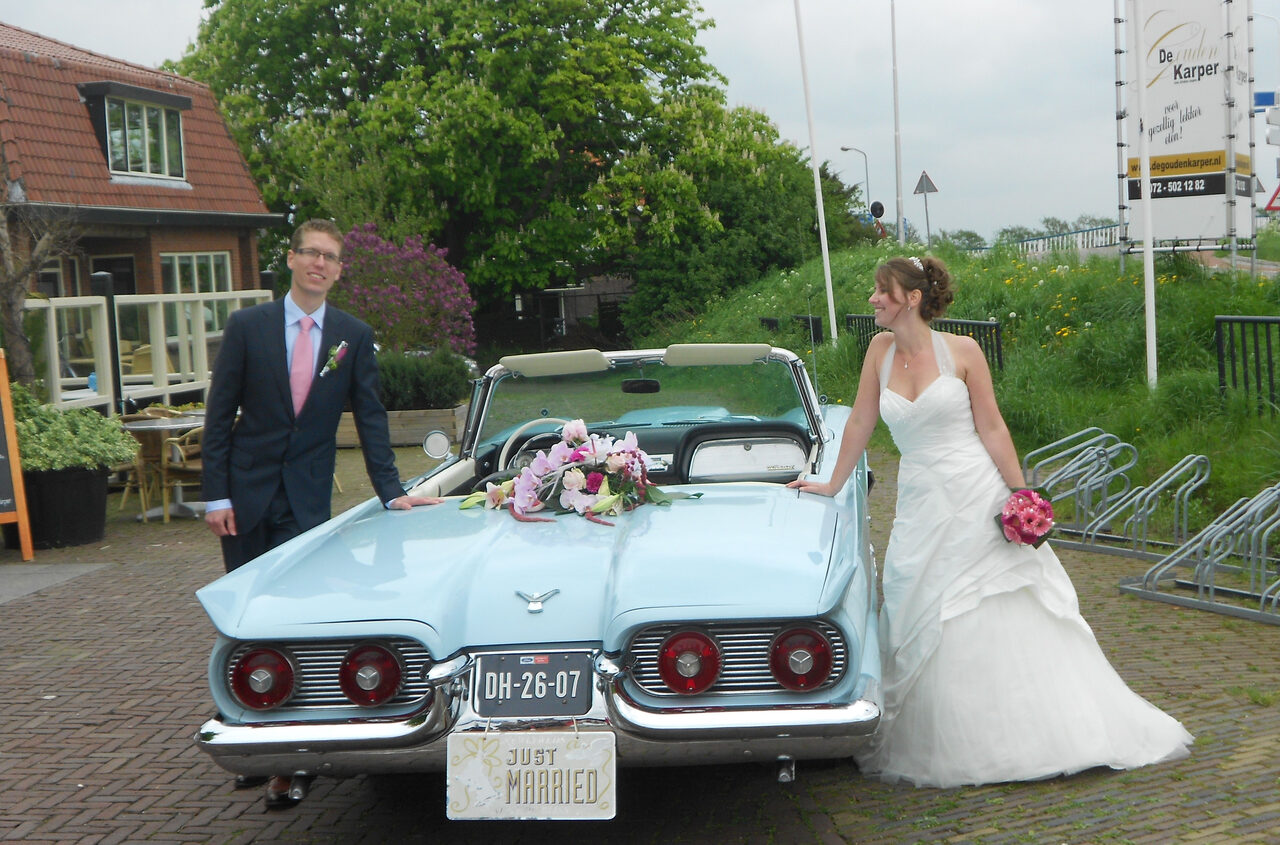 Bruidspaar bij de Ford Thunderbird 1959 met een 'Just Married'-bordje en bloemen op de motorkap.